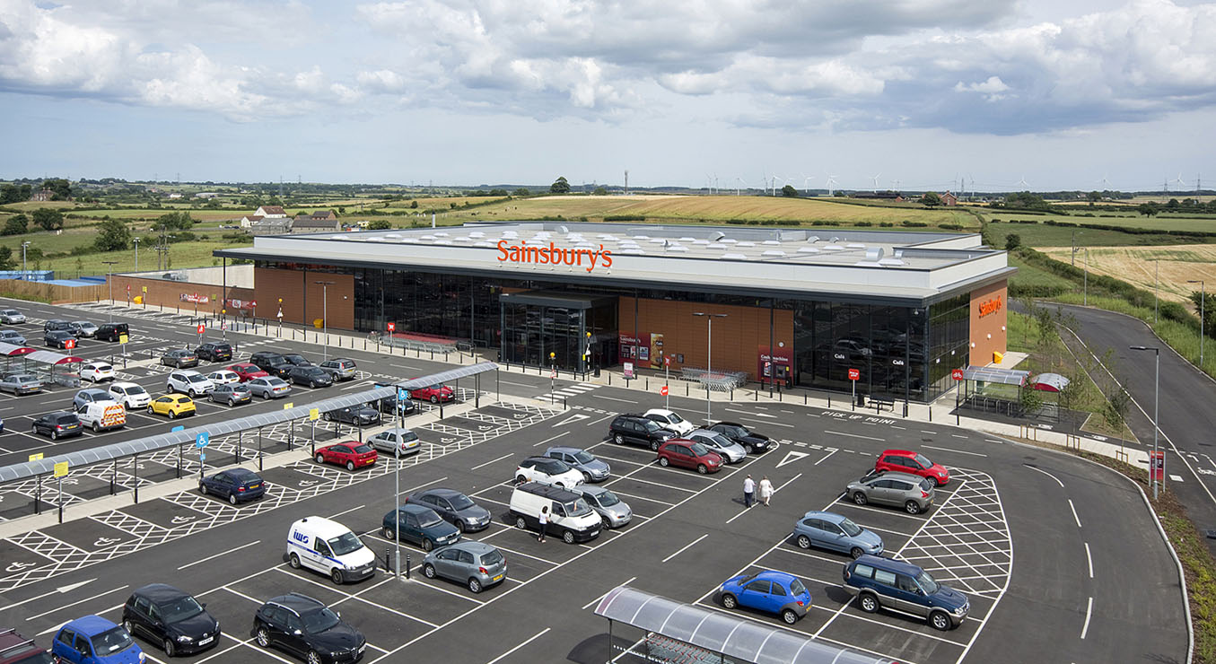 Architectural exterior view towards a retail building with car park and countryside views
