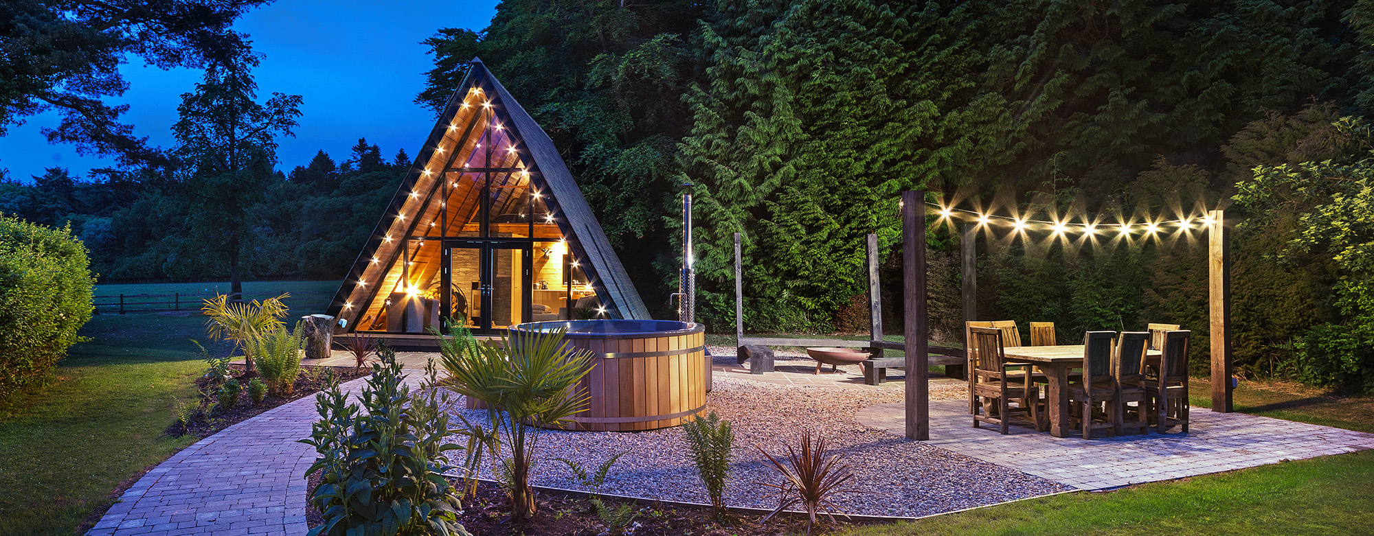 Exterior of a a-frame garden building at dusk with entertainment area