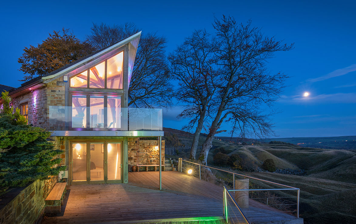 Exterior of a residential property with large glass windows overlooking the countryside at dusk