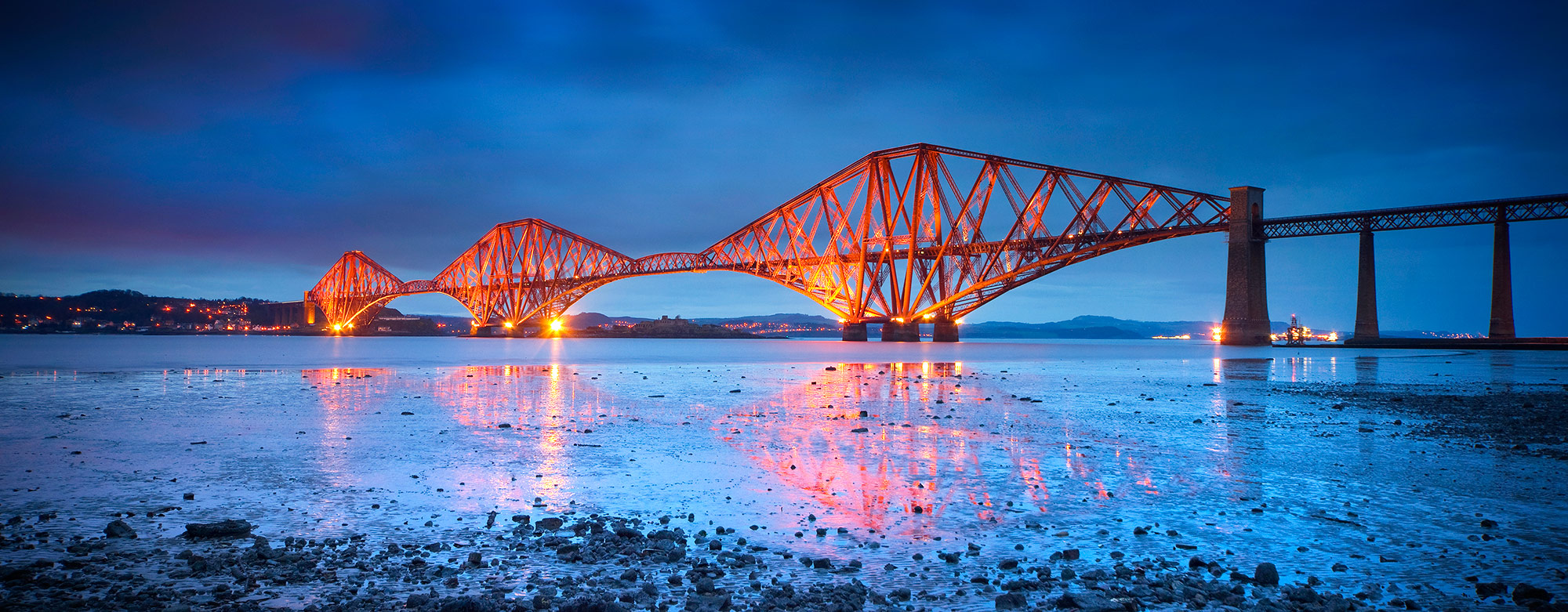 Forth Rail Bridge in Edinburgh at dusk with reflections of the bridge in the water