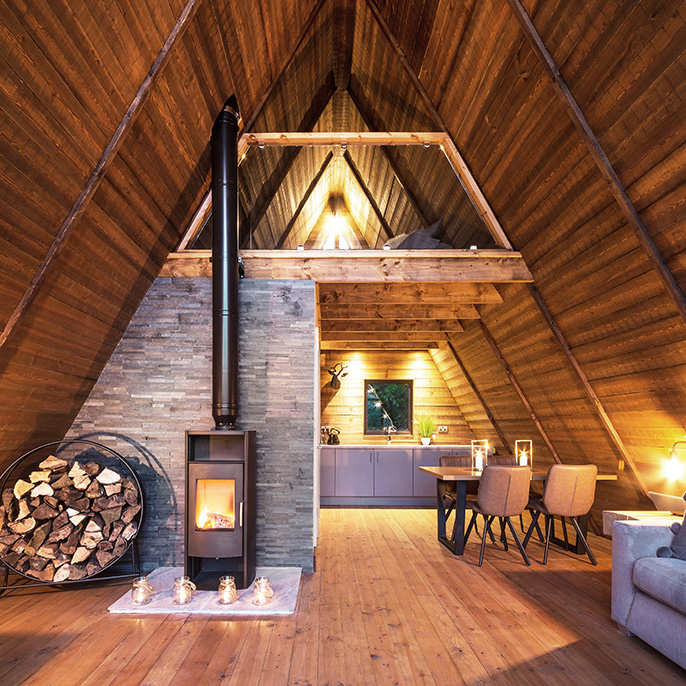 Interior of an A-frame garden building with log burning stove, kitchen and sitting area