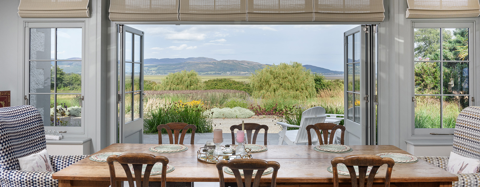 Interior of an orangery looking out over furniture towards views of garden and mountains