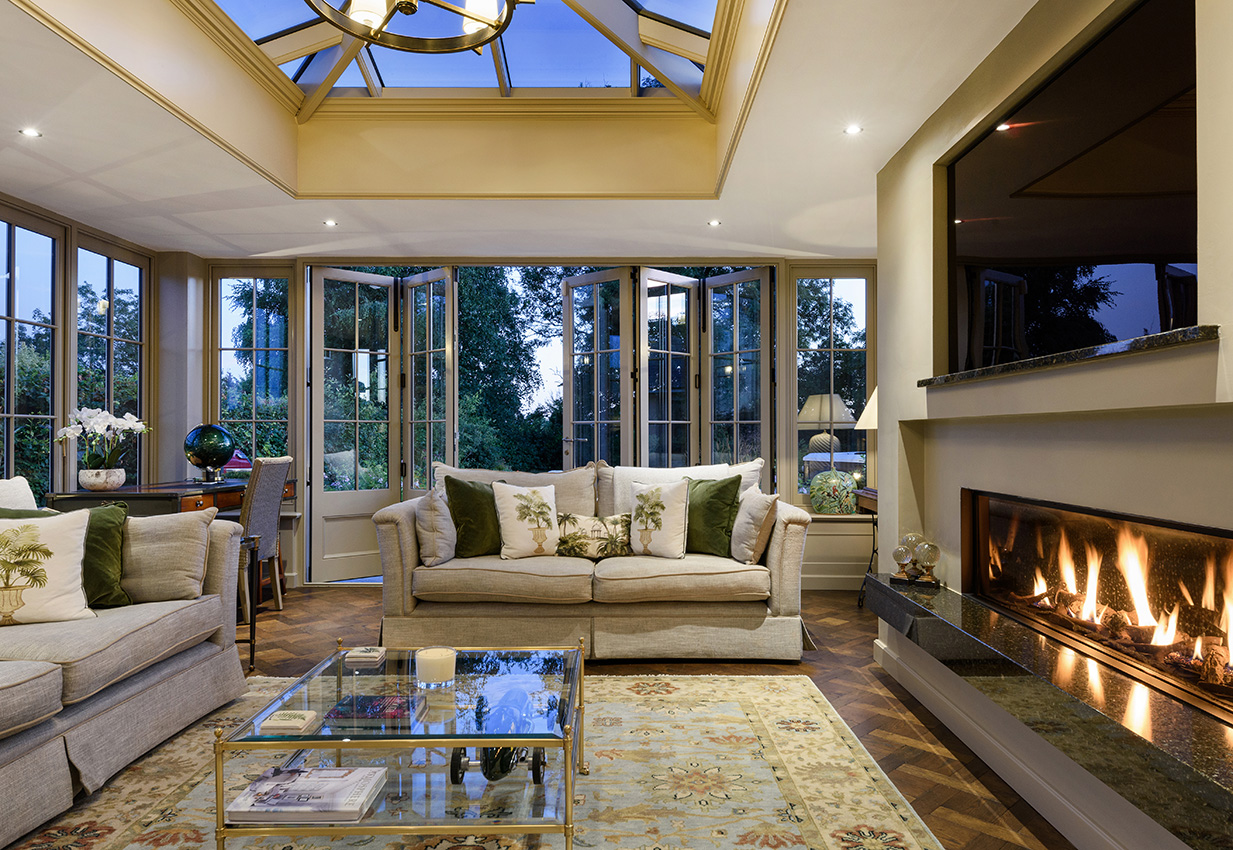 Orangery interior with a warm glowing fire and views to the garden at dusk