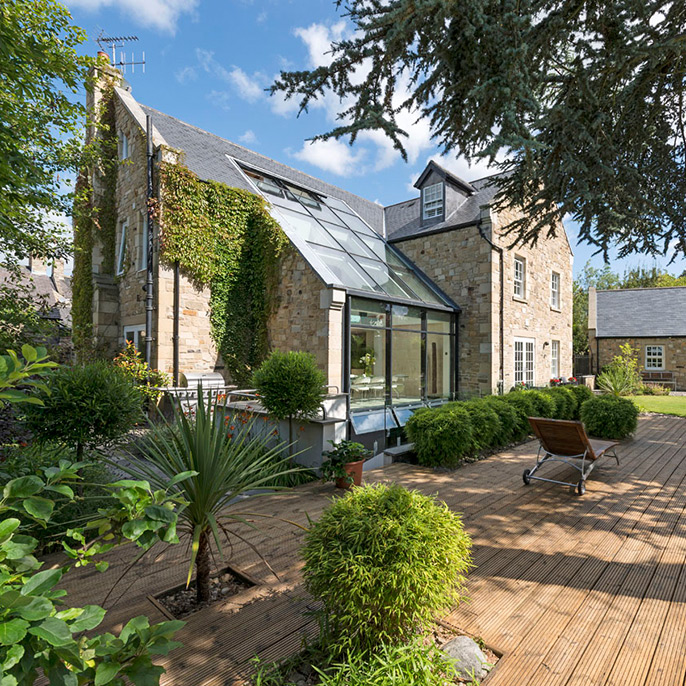 Architectural exterior of a residential property with glazed extension and decking area and garden