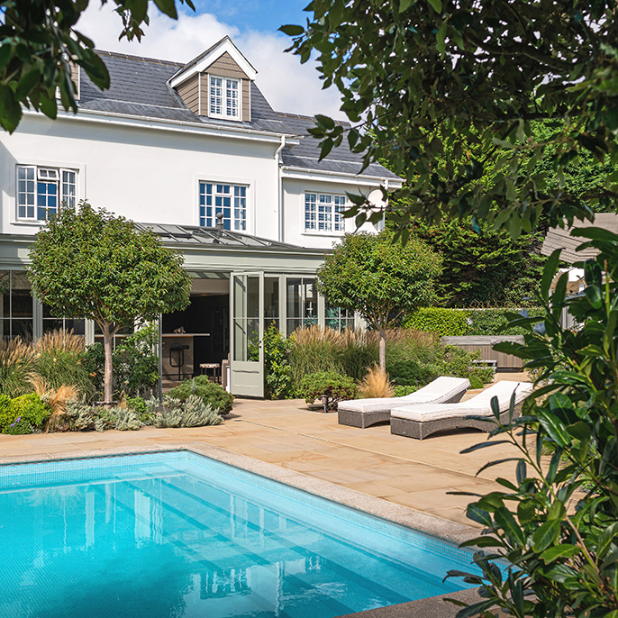 Exterior of a orangery overlooking outdoor swiming pool and gardens in summer