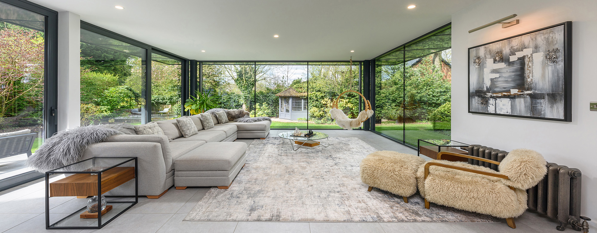 Interior of a modern spacious room looking through a glazed wall past furniture into the garden